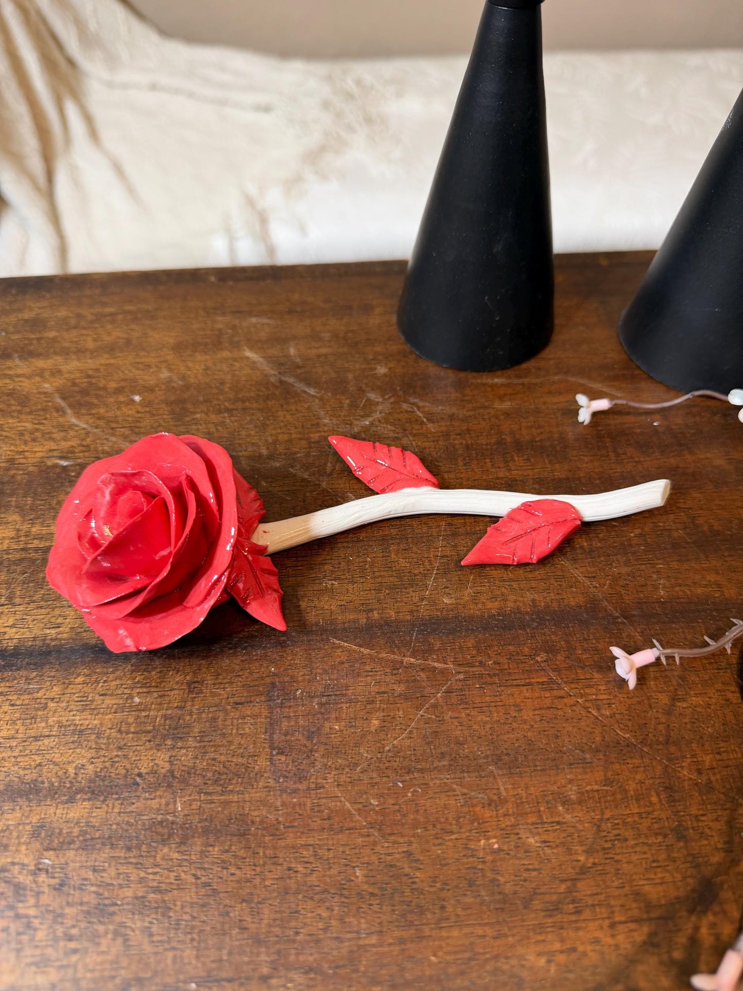 Red artificial rose on a wooden surface with black cones in the background