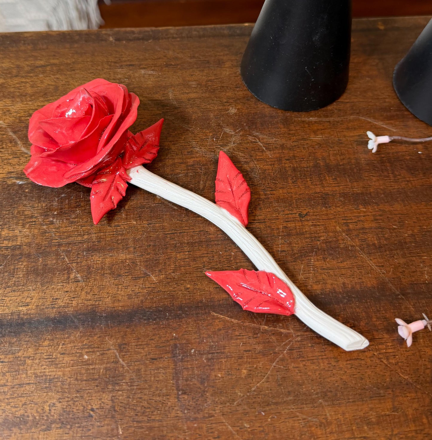 Red artificial rose on a wooden surface with black objects in the background